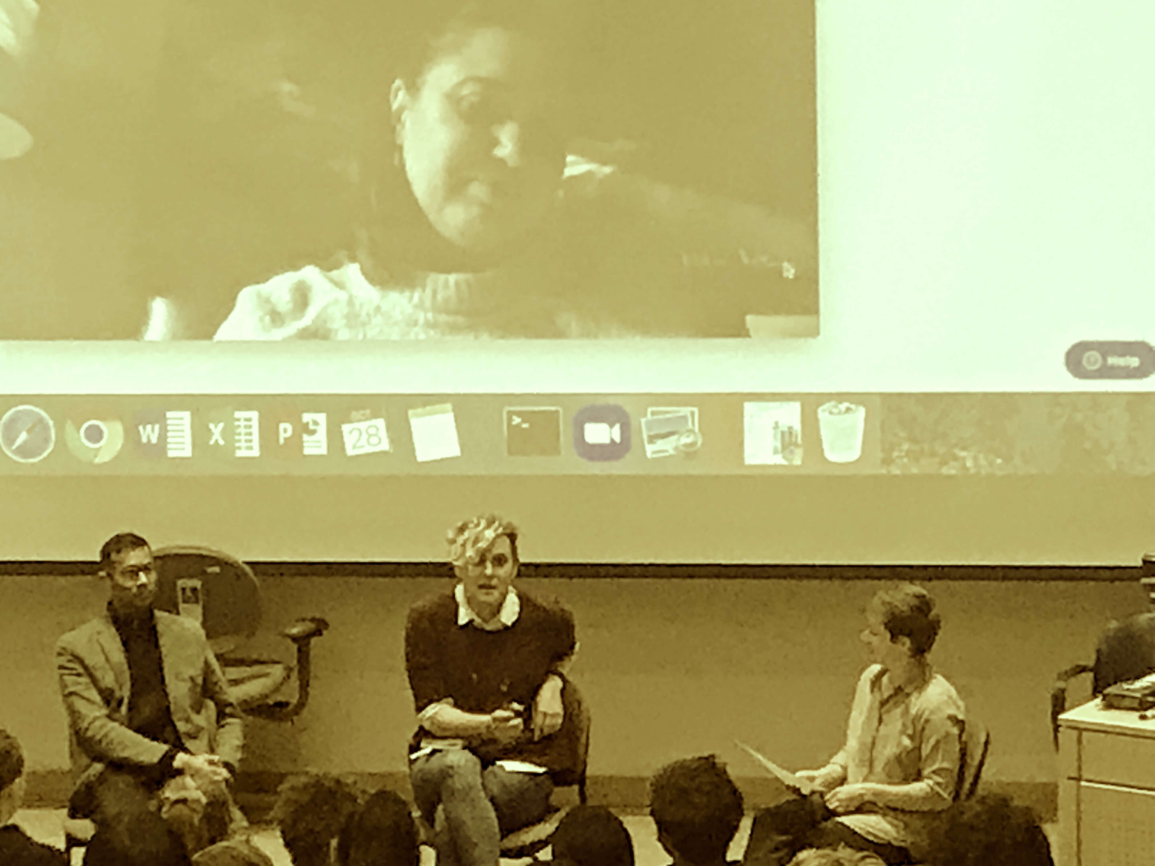 in the style of a surveillance photo: Shankar Narayan and Anna Lauren Hoffmann talk with Carissa Mayer. Ece Kamar looks down from a large screen above their heads.