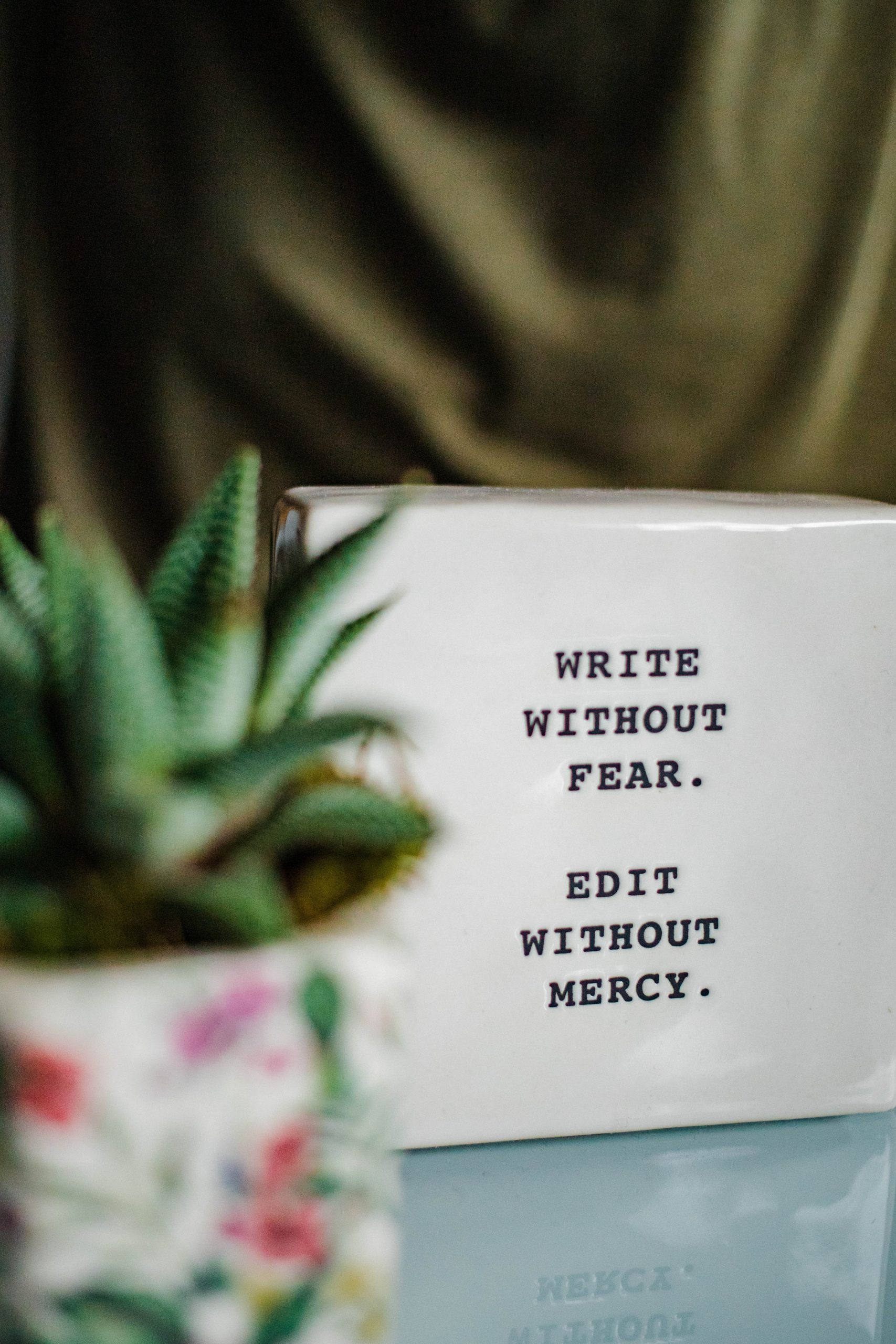 closeup of a block of glass on a desk that reads: Write without fear, edit without mercy