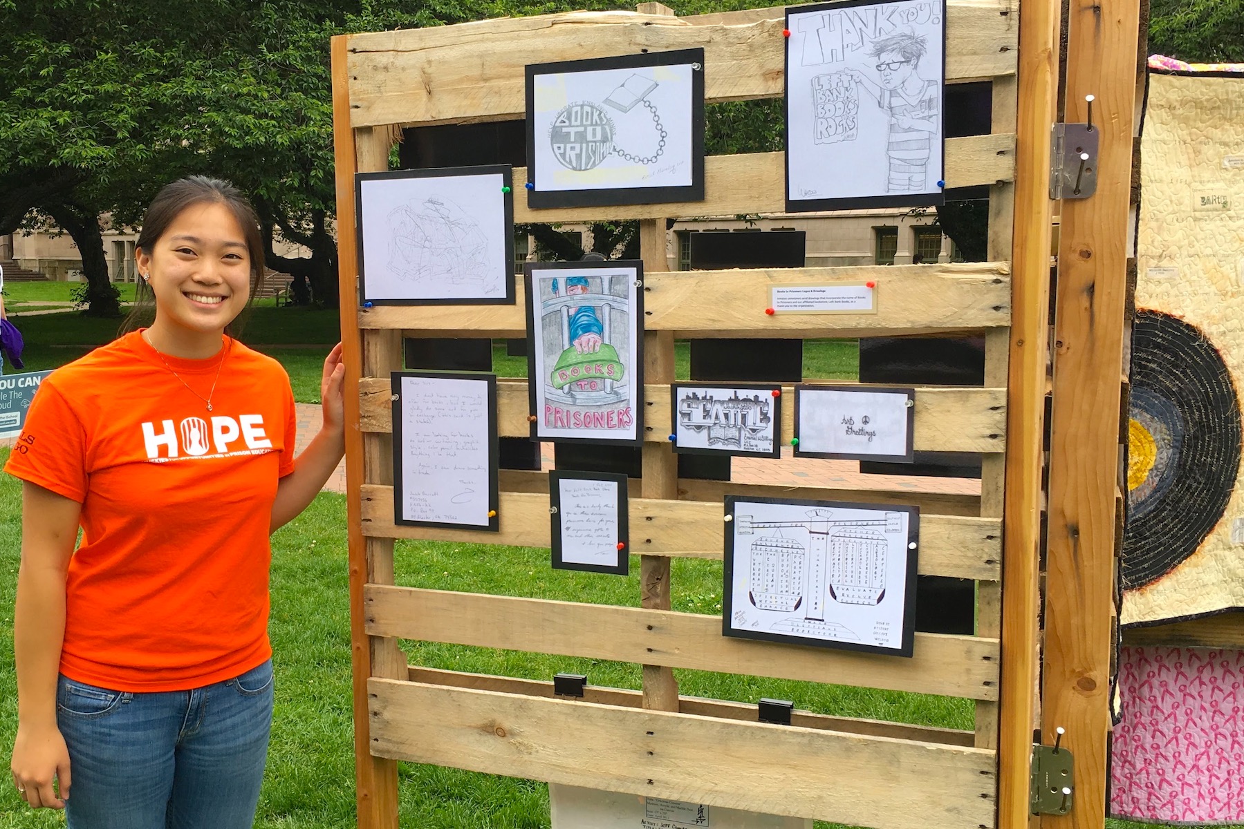 May Lim in orange HOPE T-shirt, standing next to art exhibit to raise awareness about mass incarceration issues, on UW Seattle Campus