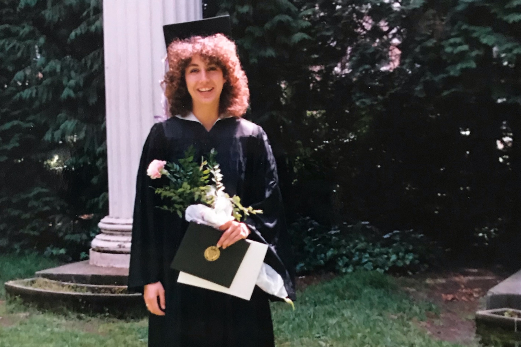 Juliana Villegas in cap & gown with flowers in UW's Sylvan Grove